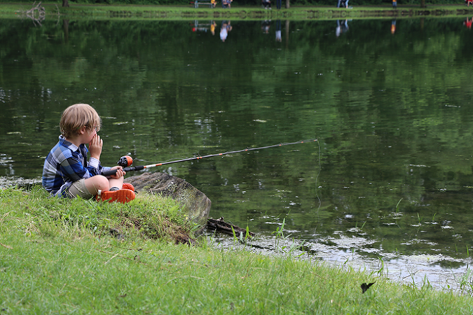 Enfant avec une canne à pêche assis au bord d'un lac