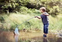Petit garçon qui pêche à l'épuisette les pieds dans l'eau
