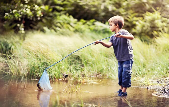 Petit garçon qui pêche à l'épuisette les pieds dans l'eau